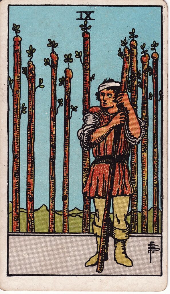 Tarotkortet Nio i stavar – en sårad man håller i en stav och blickar vaksamt – representerar uthållighet, försvar och misstro.